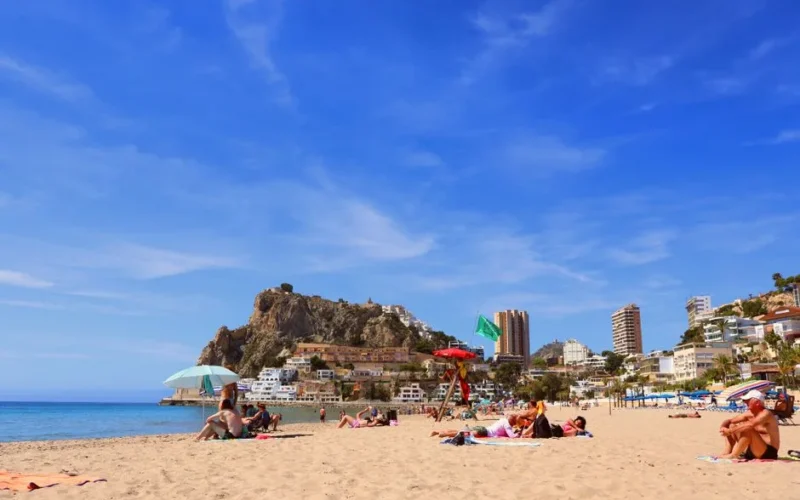 Relaxing beach in Alicante, vibrant day with clear blue skies and bustling city backdrop.