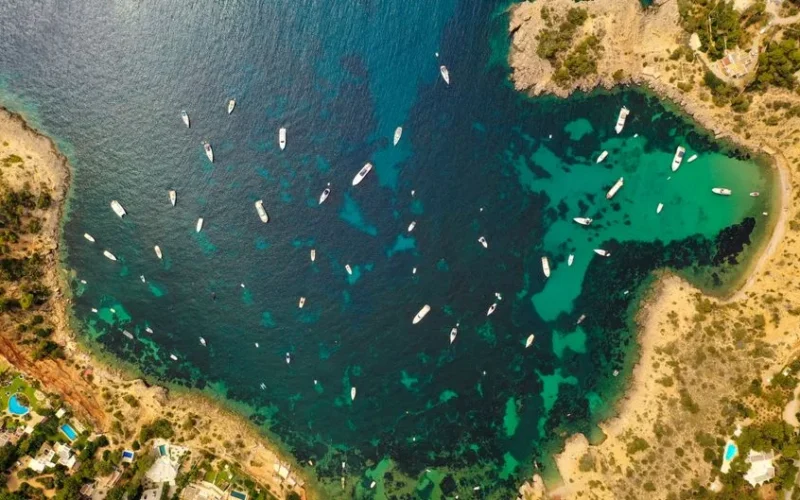 A stunning aerial view of boats in the clear turquoise waters along the coastline of Ibiza, Spain.
