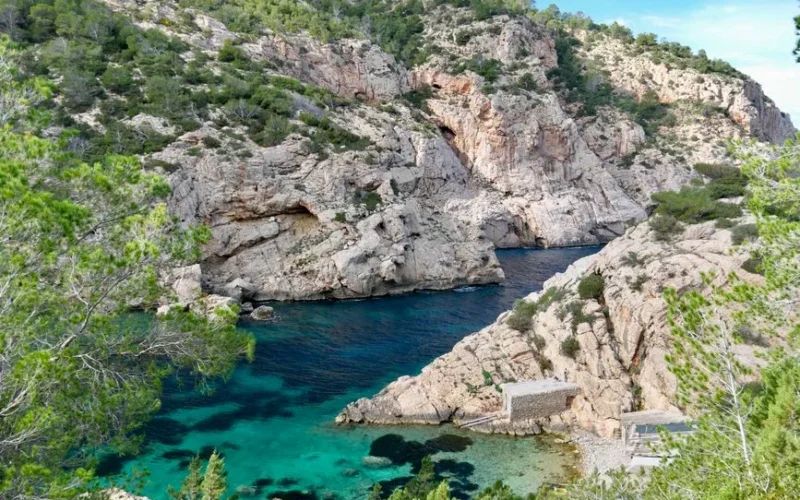 Explore a vibrant Mediterranean coastal scene with vivid turquoise waters and rugged cliffs in Ibiza, Spain.