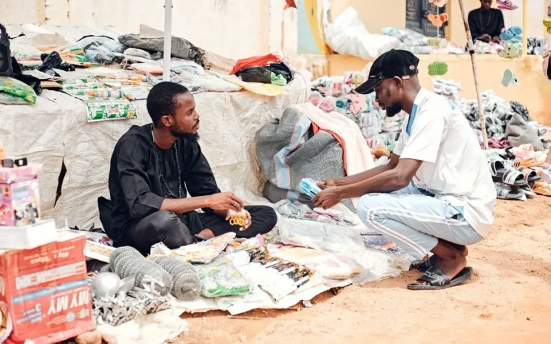 Two street vendors negotiate over goods at an outdoor market filled with various items for sale.