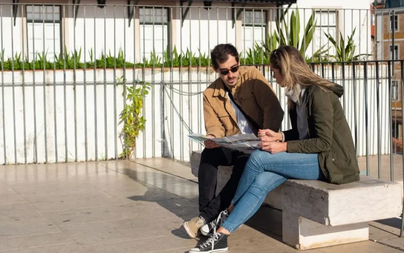 A couple of tourists sitting on a bench, studying a map on a sunny day.