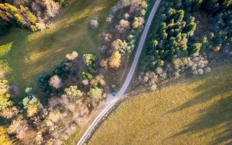 A scenic aerial view of a rural road winding through autumn forests and fields in Blechnarka, Poland.