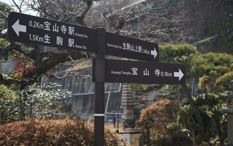 Directional signs with Japanese text point towards Hozanji Temple in a scenic Japanese setting.
