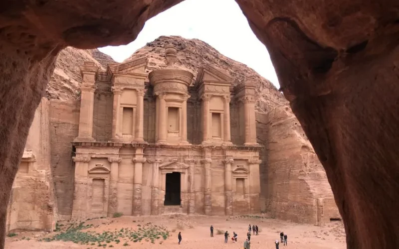 Stunning view of the ancient Al-Deir Monastery in Petra, Jordan, framed through a rock arch.