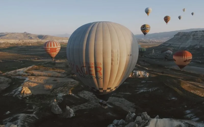 Scenic aerial view of colorful hot air balloons floating over Cappadocia's unique rock formations at sunrise.