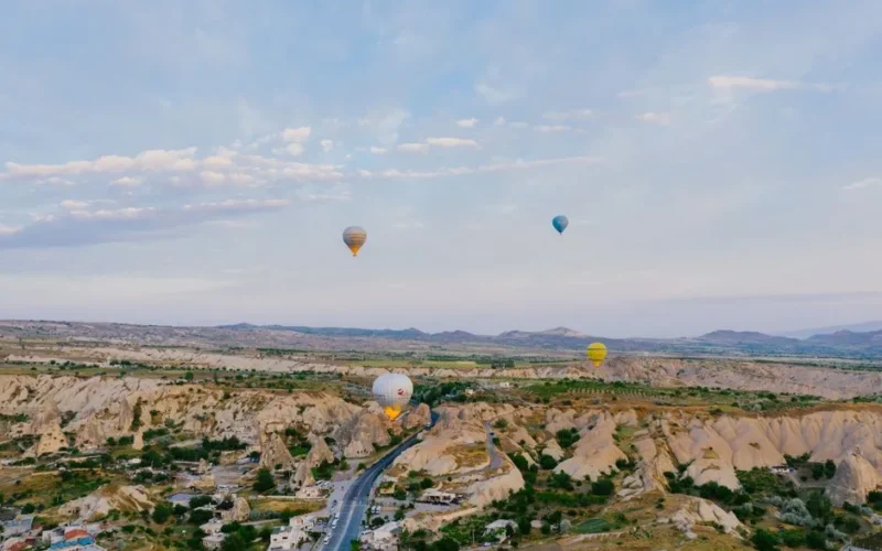 Aerial view of colorful hot air balloons soaring over the rocky landscape and road in Cappadocia, Turkey.