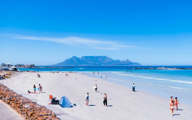 Beachgoers enjoy a sunny day at Bloubergstrand Beach, Cape Town, with Table Mountain in the background.