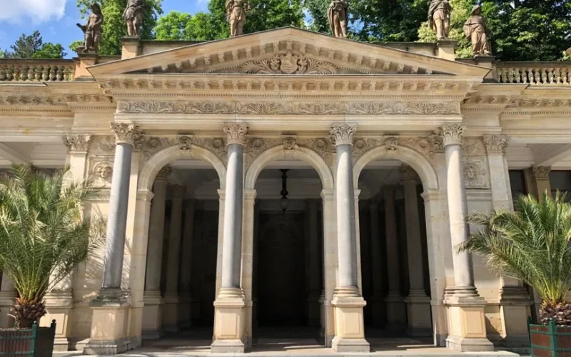 Classic Mill Colonnade in Karlovy Vary, Czechia, with ornate statues and lush greenery.