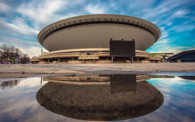 A stunning view of the Spodek Arena in Katowice, Poland, reflecting in a puddle.