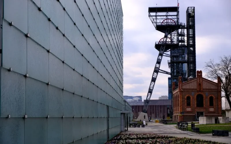 A juxtaposition of modern glass architecture and historic brick buildings in an urban industrial area.