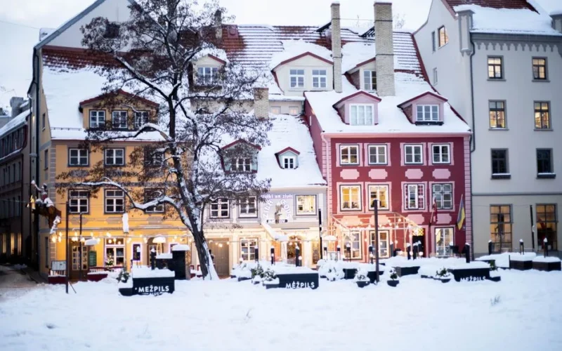 Charming snow-covered facades and glowing lights in Riga's town square captured during winter.