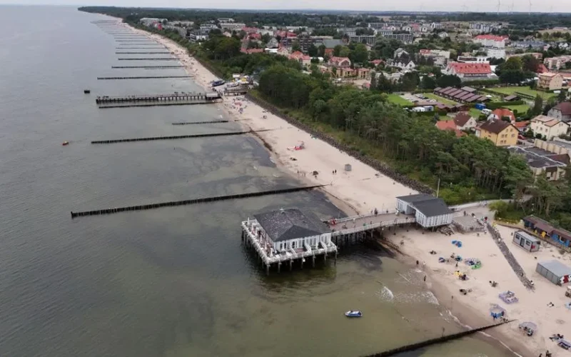 Aerial shot of a coastal town with beach, pier, and waterfront buildings.