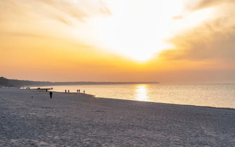 Experience the serene beauty of a sunset at Kołobrzeg Beach, showcasing vibrant colors and tranquil waves.