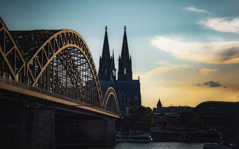 Sunset scene of Cologne Cathedral and Hohenzollern Bridge over the Rhine River in Germany.