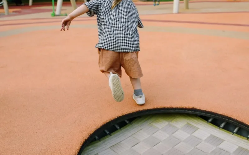 A playful child jumping on a trampoline at an outdoor playground during summer.