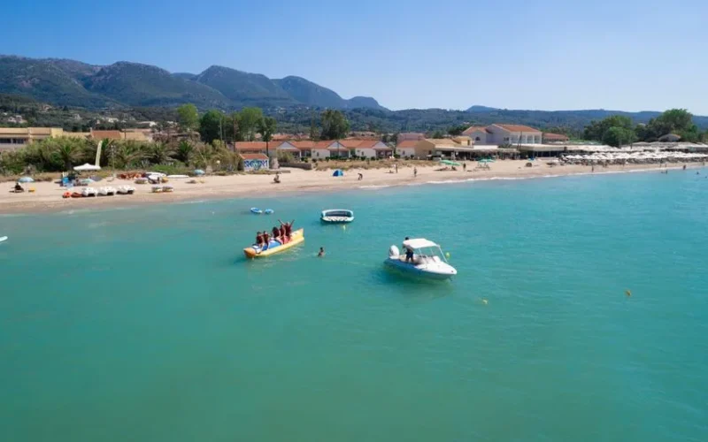 Turquoise sea and vibrant beach scene in Corfu, Greece, capturing summer fun and water activities.