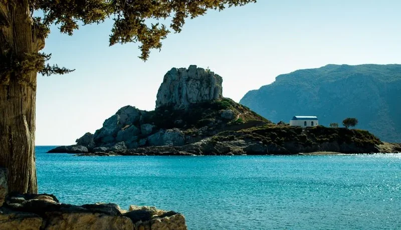 Beautiful coastal view of Kos, Greece featuring a rocky island and vibrant blue waters.