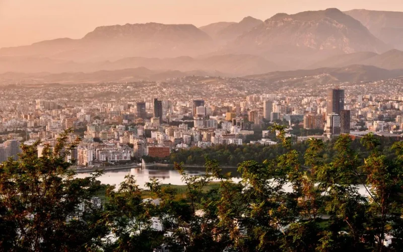 A stunning aerial view of Tirana's skyline framed by mountains and lush greenery during sunset.