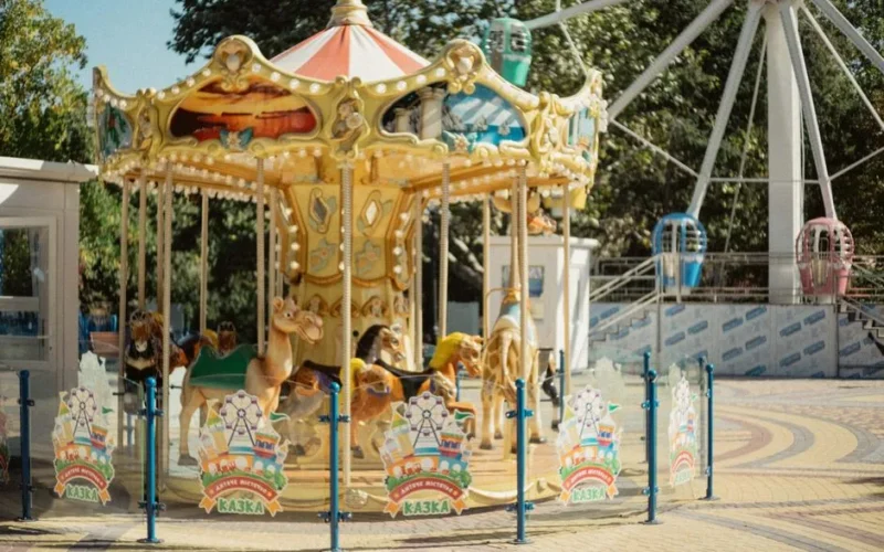 Colorful carousel at an outdoor amusement park, featuring animal rides in a summer setting.