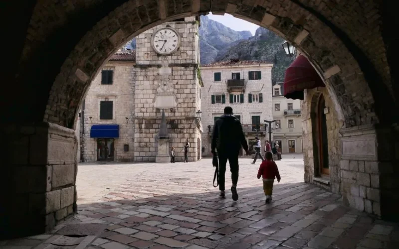 A father and child walking through a historic archway in Kotor, Montenegro's old town square.