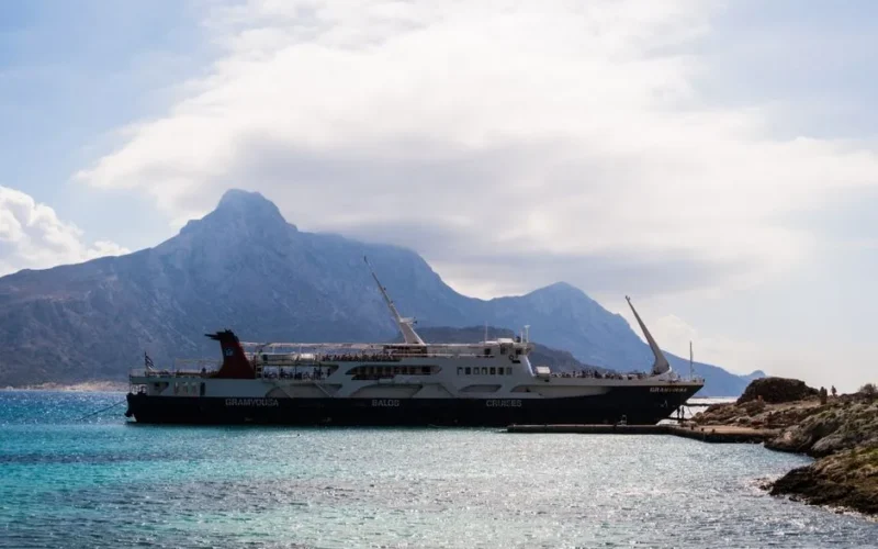Ferry docked at the picturesque Balos Beach, Greece with a mountainous backdrop.