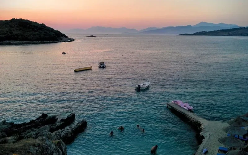Golden sunset over Ksamil beach with swimmers and boats in a tranquil seascape.
