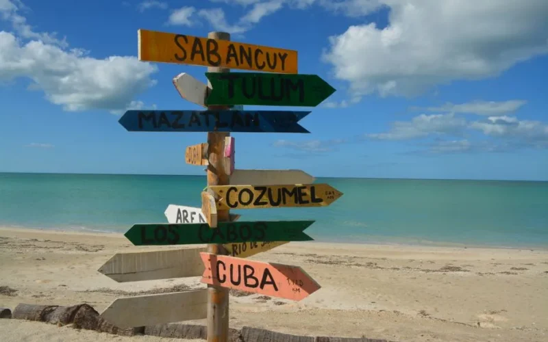 Colorful signpost on a sunny beach, pointing to popular vacation destinations.