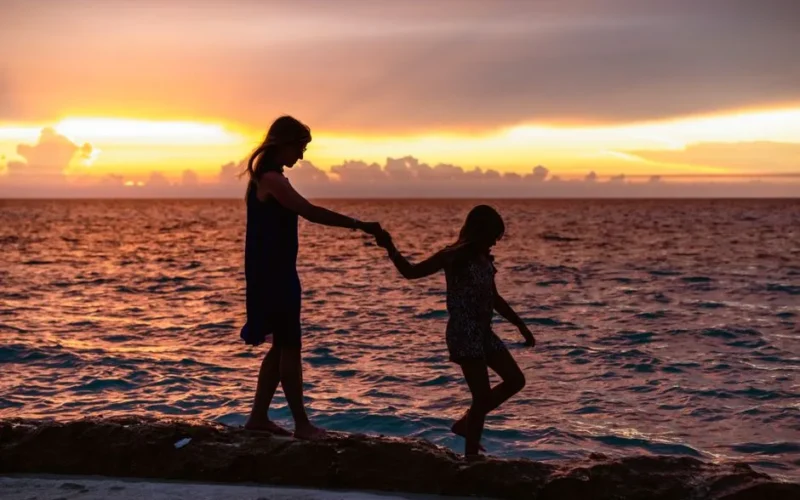 A mother and daughter hold hands walking along the beach at sunset in Varadero, Cuba.