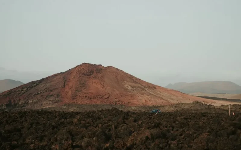 Explore the rugged volcanic terrain of Lanzarote, featuring a prominent red-hued mountain.