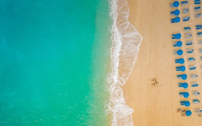 A stunning aerial capture of Lefkada beach with turquoise waters, blue umbrellas, and soft golden sand.