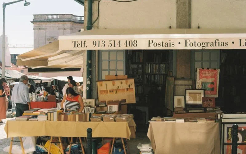 Colorful street market in Lisbon with a book stand displaying items on a sunny day.