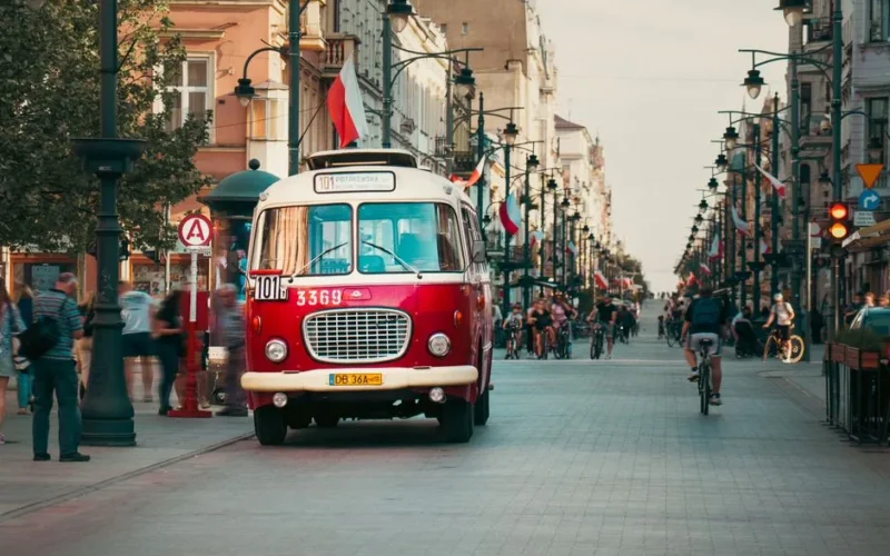Historic red bus in motion on Piotrkowska Street, Łódź, Poland, showcasing urban city life.