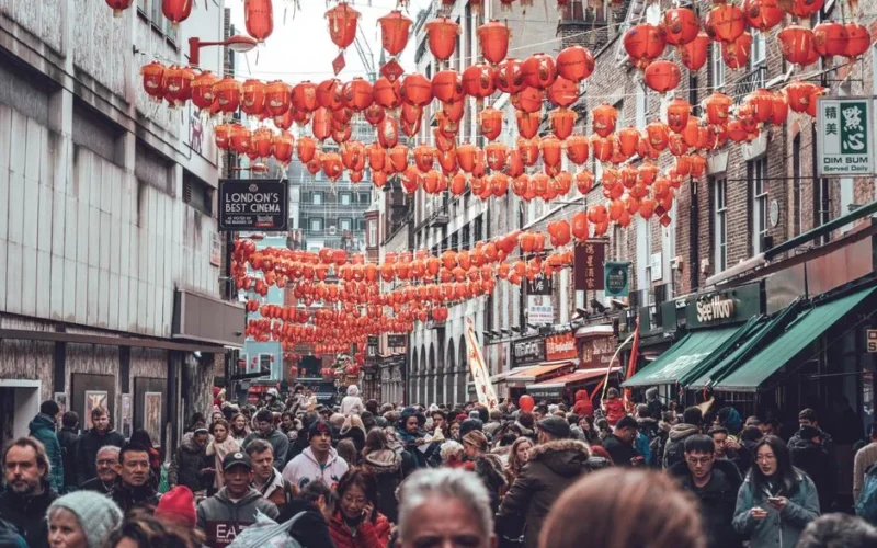 Crowded street in London's Chinatown adorned with traditional red lanterns, capturing vibrant cultural atmosphere.