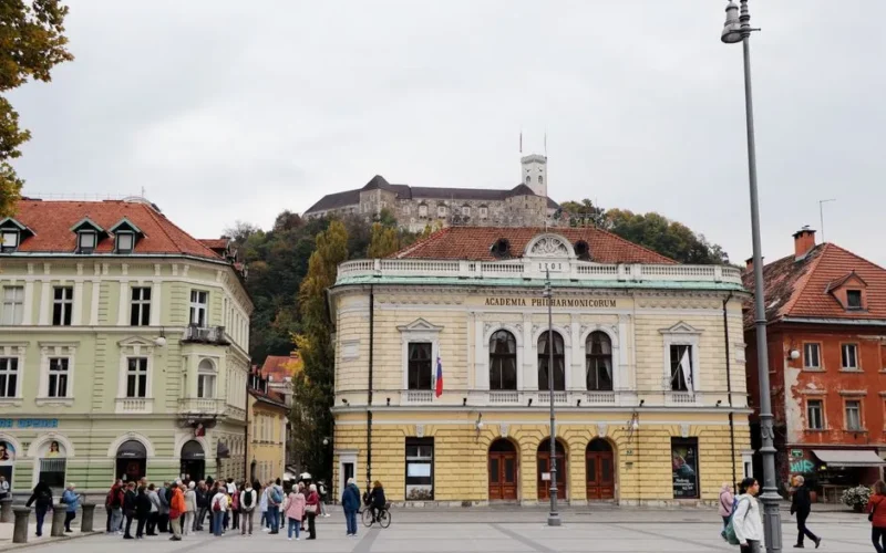 Scenic view of historical Ljubljana Castle from a bustling city square with architectural buildings.