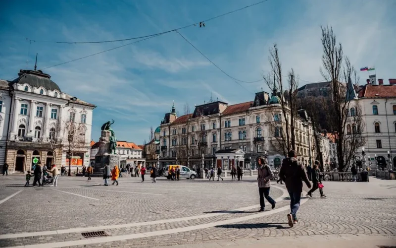 People enjoying a sunny day at Prešeren Square, Ljubljana. Historic architecture and vibrant urban life.