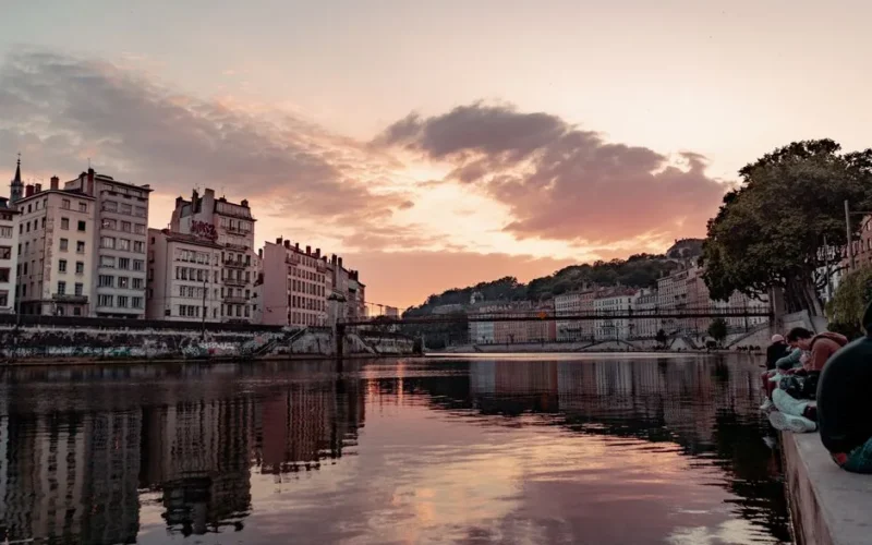 Beautiful sunset view over the Saone River in Lyon, France, showcasing urban townhouses and reflections.