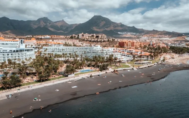 Scenic aerial shot of Adeje's beachside resorts with majestic mountains as a backdrop on a sunny day.
