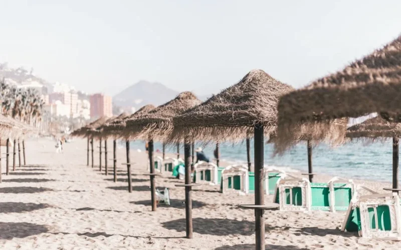 A serene sandy beach with straw umbrellas and clear skies, perfect for a summer vacation in Malaga, Spain.