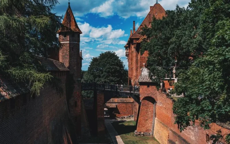 Explore the historic and majestic medieval Malbork Castle in Poland with towering walls and lush trees.