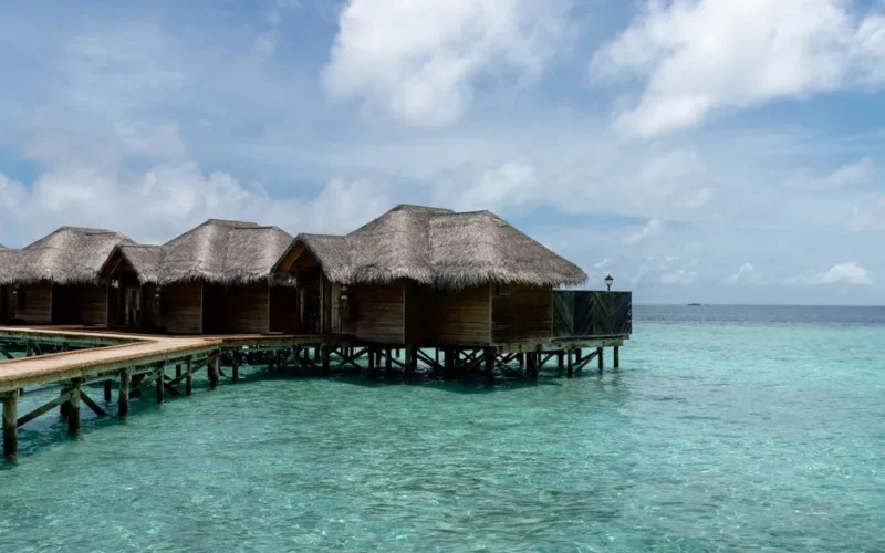 Overwater bungalows with thatched roofs on a turquoise ocean, under a clear blue sky in the Maldives.