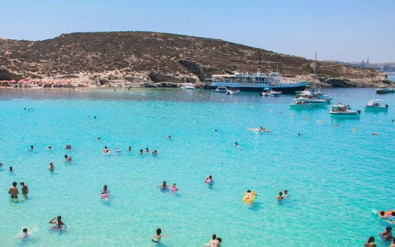 Idyllic scene of swimmers and boats at Malta's Blue Lagoon on a sunny summer day.