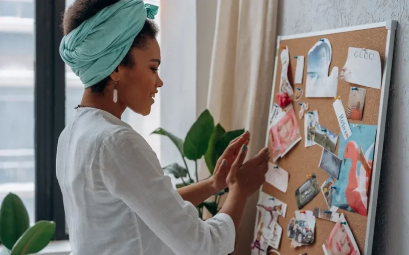 A woman arranging a creative mood board with diverse images and notes in a stylish interior.