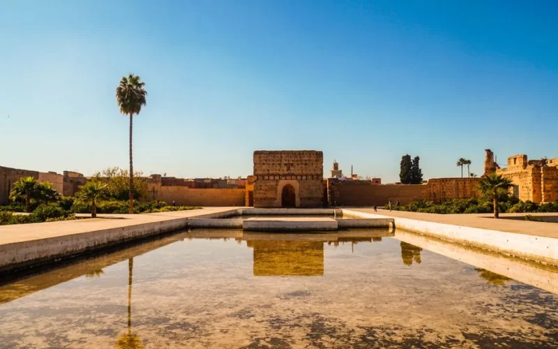 El Badi Palace in Marrakech under a clear blue sky with a reflecting pool in the foreground.