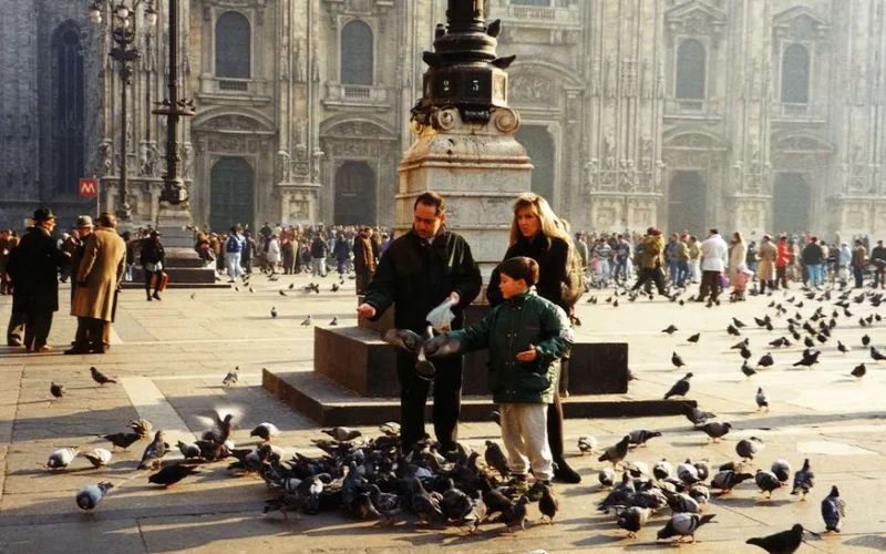 A family enjoys feeding pigeons at Piazza del Duomo, Milan, in front of the historic cathedral.