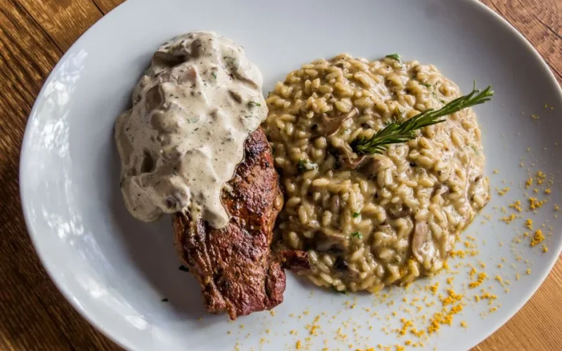 Delicious steak topped with sauce served with creamy mushroom risotto. Italian cuisine on a white plate.