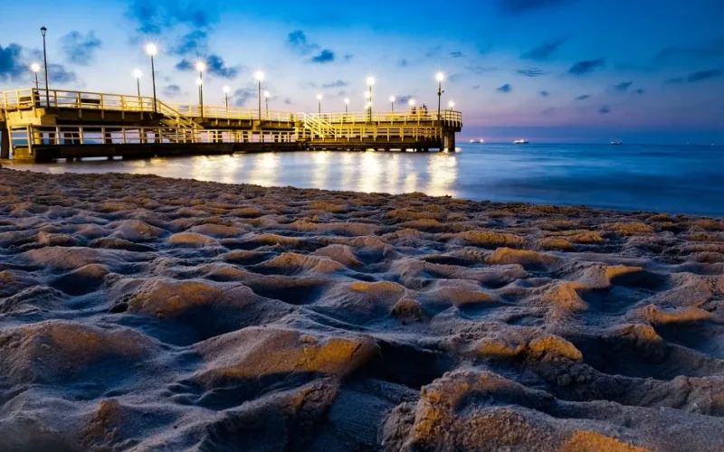 A serene evening view of the illuminated pier on the sandy beach in Gdańsk, Poland.
