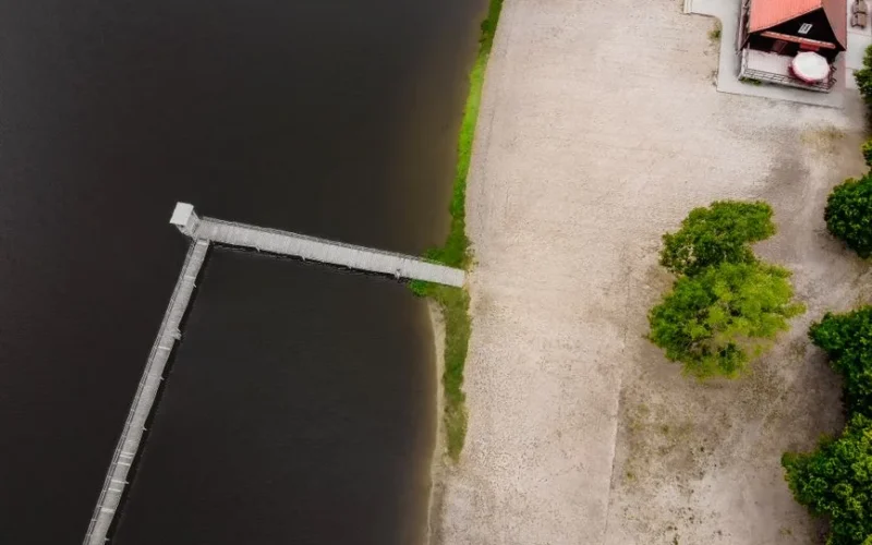 A drone shot capturing a peaceful lakeside pier and sandy beach in Zaniemyśl, Poland from above.