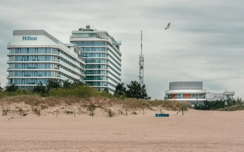 A contemporary Hilton hotel by the sandy beach in Świnoujście, Poland, with a cloudy sky backdrop.