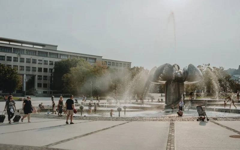 People enjoy a sunny day at a city fountain with mist and playful water jets.