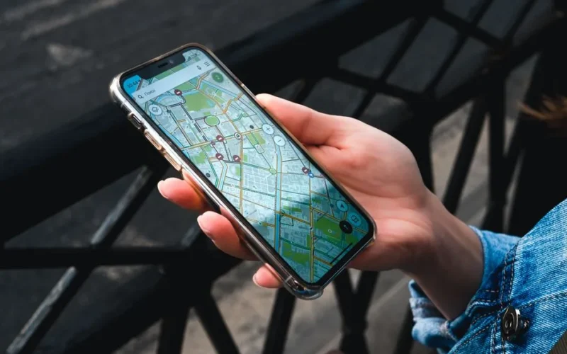 An outdoor close-up of a hand holding a smartphone displaying a map application.